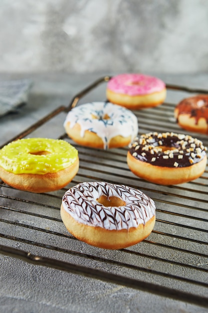 Veelkleurige donuts met glazuur en hagelslag op een metalen standaard uit de oven en een grijs servet.