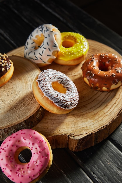 Veelkleurige donuts met glazuur en hagelslag op houten onderzetters op een zwarte achtergrond.