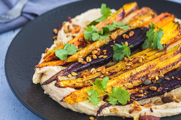 Veelkleurige gebakken wortelen met hummus op zwarte plaat Veganistisch recept