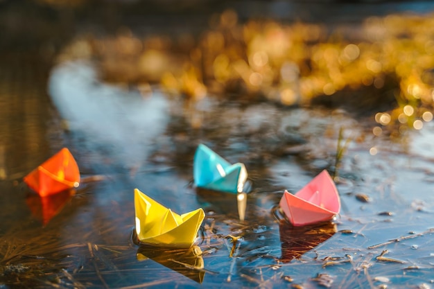 Veelkleurige papieren boten Kleurrijk roze geel blauw oranje schepen in grote lente sneeuw plas op winter straat Warm nat regenachtig weer oud gras Hallo lente herfst Kinderen spelen veel plezier buitenshuis