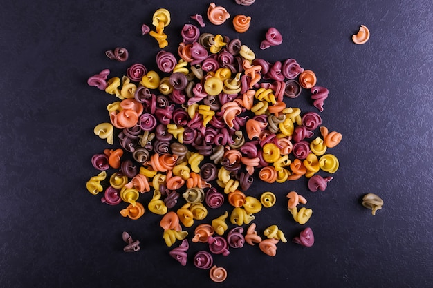 Veelkleurige pasta met de toevoeging van natuurlijke plantaardige kleurstof verspreid over een zwarte betonnen tafel. bovenaanzicht,.