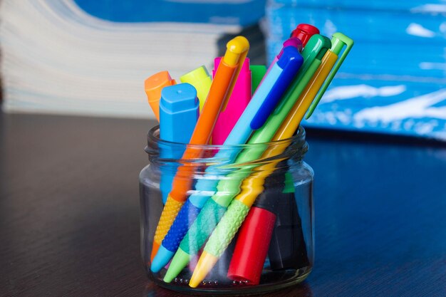 Veelkleurige pennen en stiften in een standaard op de achtergrond van stack of notebooks pack of blue