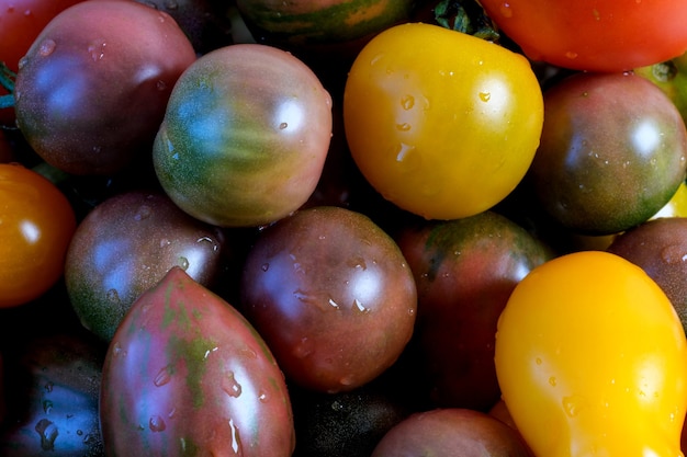 Veelkleurige rijpe kleine tomaten van verschillende variëteiten liggen op een houten tafel close-up macrofotografie