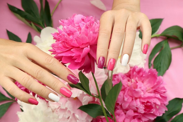 Veelkleurige roze en bordeauxrode manicure op een achtergrond van pioenrozen