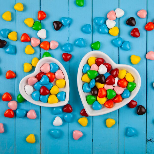 Veelkleurige snoepjes in een bord in de vorm van een hart op een blauwe houten achtergrond. Valentijnsdag.