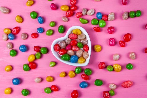 Veelkleurige snoepjes in een bord in de vorm van een hart op een roze houten ondergrond. Valentijnsdag.