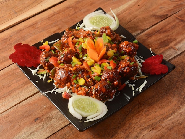 Veg Manchurian Popular indochinese food made of cauliflower florets and other vegetable served in a black plate over a rustic wooden table selective focus