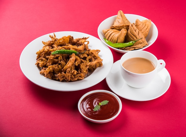 Photo veg samosa - is a crispy and spicy indian triangle shape tea time snack. served with fried green chilly, onion & chutney or ketchup. over colourful or wooden background. selective focus