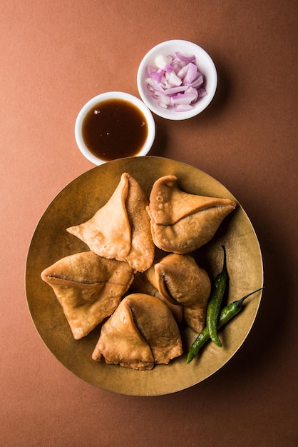 Veg samosa - è uno snack indiano croccante e speziato a forma di triangolo per l'ora del tè servito con peperoncino verde fritto, cipolla e chutney o ketchup