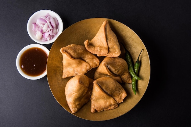 Veg samosa - è uno snack indiano croccante e speziato a forma di triangolo per l'ora del tè servito con peperoncino verde fritto, cipolla e chutney o ketchup