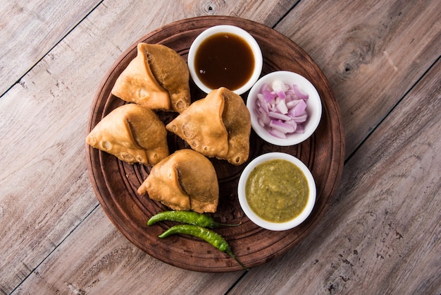 Veg Samosa - is een knapperige en pittige Indiase driehoekige theetijdsnack. Geserveerd met gebakken groene peper, ui & chutney of ketchup