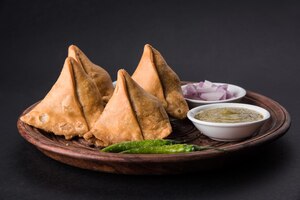 Foto veg samosa - is een knapperige en pittige indiase driehoekige theetijdsnack. geserveerd met gebakken groene peper, ui & chutney of ketchup