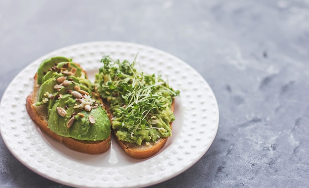 Vegan avocado sandwich met microgreens op een witte plaat op een grijze ondergrond