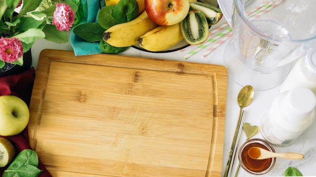 Vegan background Various fruits and blender around cutting wooden board