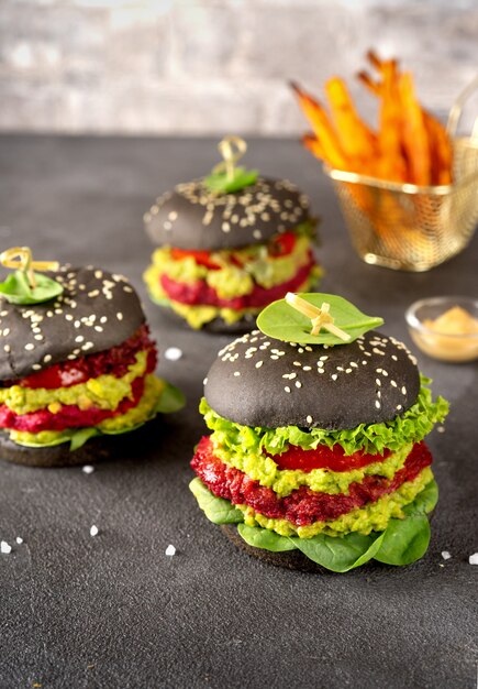 Vegan black burgers with beet patties and avocado on dark surface