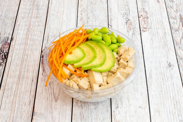 Vegan bowl van Hawaïaanse poke met plakjes Mexicaanse avocado Japanse edamame bonen geraspte wortelen en veel tofu taco's op een transparante meeneemdoos