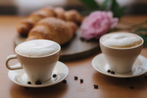 Vegan breakfast at home Cappuccino with coconut milk and two empty vegan croissants Morning with coffe Pink peony flower on table