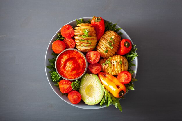 Vegan buddha bowl. healthy lunch bowl with hasselback potato, avocado, tomato, bell peppers and pepper sauce