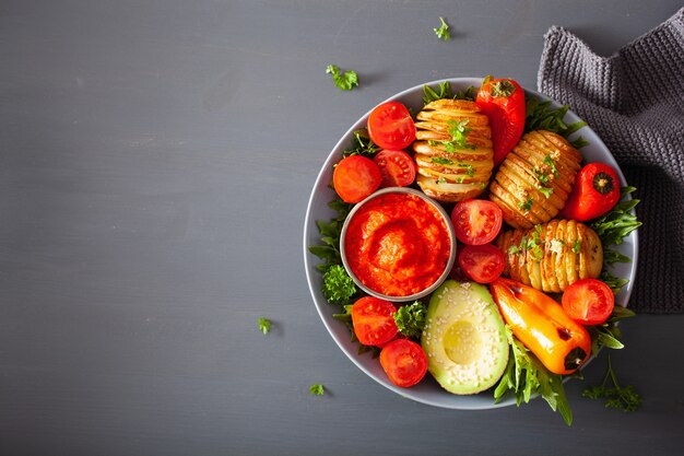 Vegan buddha bowl. healthy lunch bowl with hasselback potato, avocado, tomato, bell peppers and pepper sauce