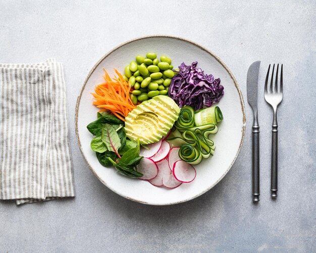 Vegan buddha bowl with avocado edamame beans cucumber red cabbage carrots radishes and spinach veget