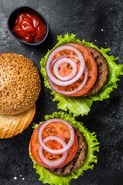 Vegan burger with Plant based meatless cutlets patties tomato and onion Black background Top view