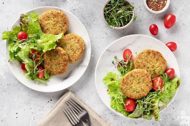 Vegan burgers with quinoa, broccoli and salad in plates on light marble background