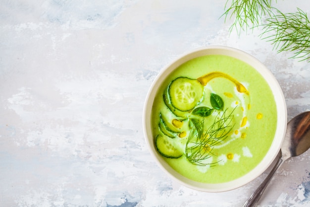 Vegan cold cucumber cream soup in white bowl on a gray 