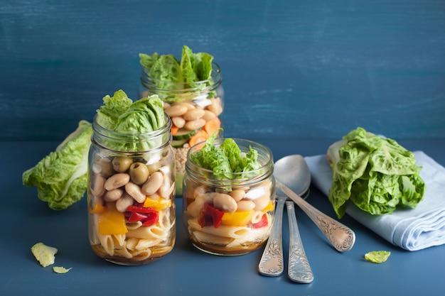 Vegan couscous and pasta salad in mason jars with vegetables beans