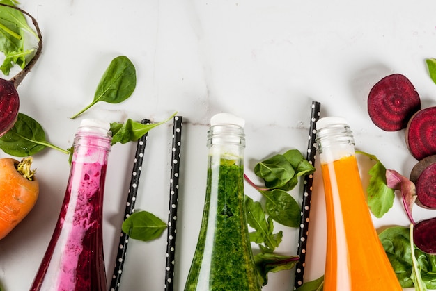 Vegan diet food. Selection colorful fresh organic smoothies drinks with autumn vegetables: beetroot, pumpkin, carrot, leafy vegetables. In bottles, white table.  top view