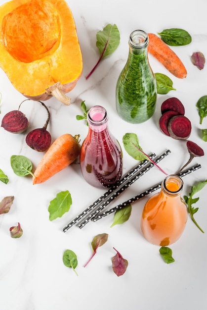 Vegan diet food. Selection colorful fresh organic smoothies drinks with autumn vegetables: beetroot, pumpkin, carrot, leafy vegetables. In bottles, white table.  top view