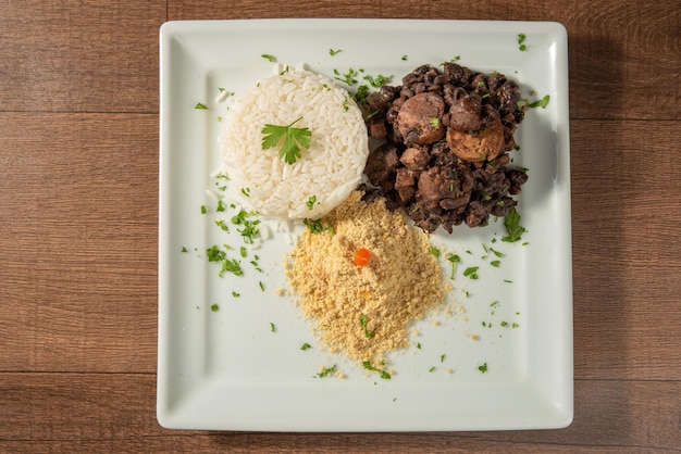 Vegan food vegan feijoada rice and farofa on a white plate over wood top view