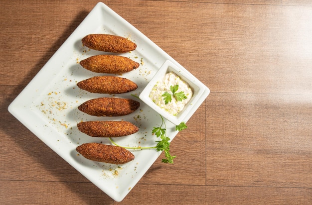 Vegan food vegan kibbeh and sauce on a white plate over wood top view