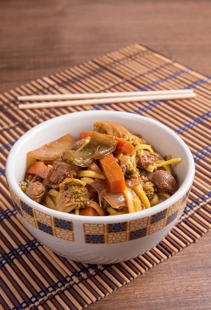 Vegan food vegan yakisoba with chopsticks in a bowl on bamboo\
mat over wood selective focus