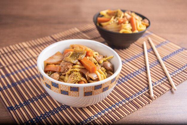 Vegan food vegan yakisoba with chopsticks in a bowl on bamboo
mat over wood selective focus