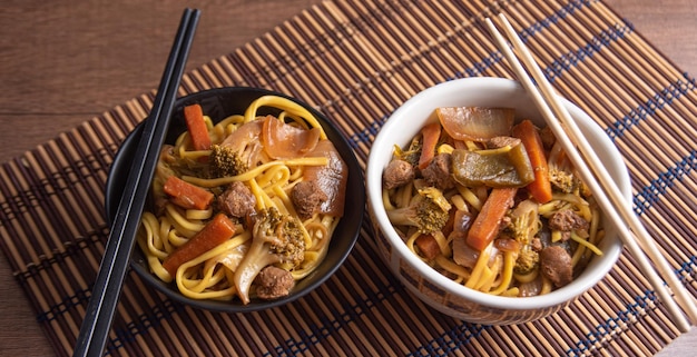 Vegan food Vegan Yakisoba with chopsticks in a bowl on bamboo mat over wood selective focus