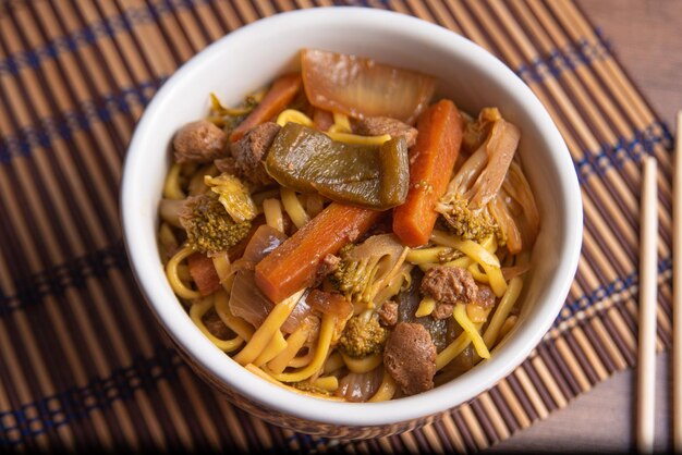 Vegan food vegan yakisoba with chopsticks in a bowl on bamboo
mat over wood top view