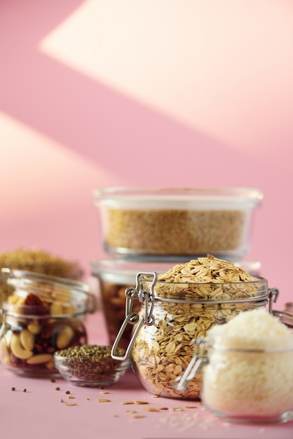 Vegan health food over pink background with copy space. Nuts, seeds, cereals, grains in glass jars. 