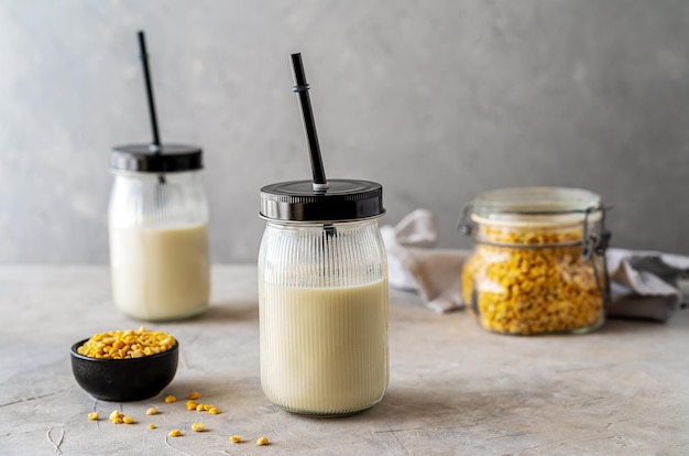 Vegan healthy pea milk in glass jars with drinking straws concrete background pea grains. Mockup