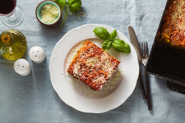 Vegan lasagne met linzen en groene erwten in een bakplaat op een tafel met een blauw linnen tafellaken. en rode wijn in glazen