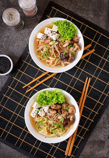 Vegan noedel soep met tofu kaas, shiitake champignons en sla in witte kom.