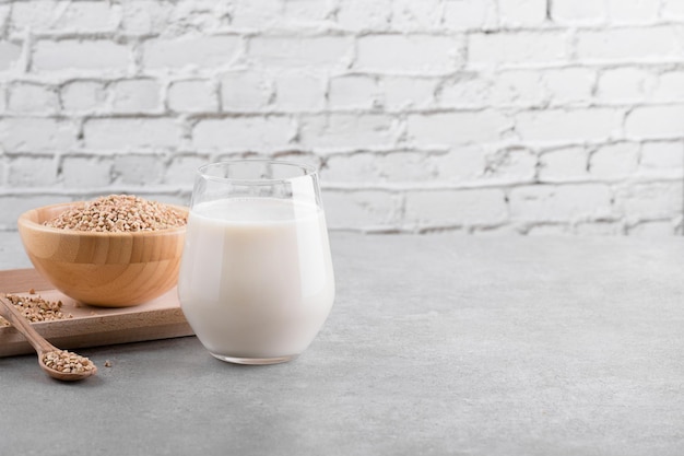 Vegan non diary buckwheat milk in glass with wooden bowl with buckwheat groats on a grey stone table Vegan buckwheat drink is plant based alternative milk  Veggies healthy milk product copy space
