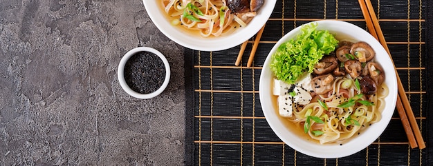 Vegan noodle soup with tofu cheese, shiitake mushrooms and lettuce in white bowl. Asian food. Top view.  Flat lay