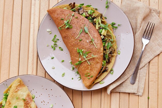 Vegan pancakes filled with mushrooms pea sprouts and avocado Healthy breakfast for two persons on the wooden table