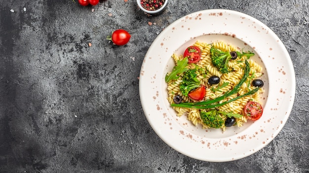 Vegan Pasta salad with tomato, broccoli, black olives, and asparagus. banner, menu recipe place for text, top view.