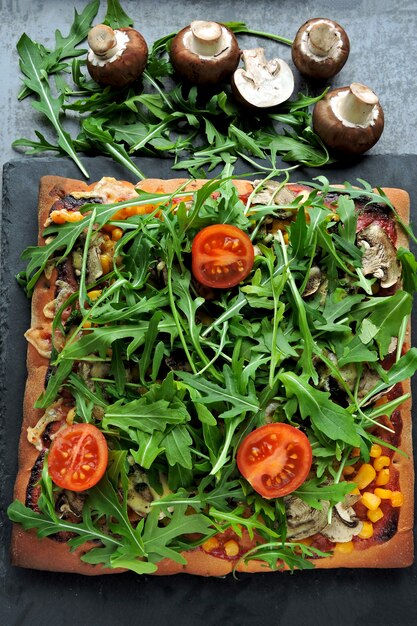 Vegan pizza with mushrooms and fresh arugula. Square pizza with vegetables, mushrooms and arugula.