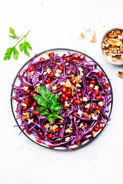 Vegan red cabbage salad with parsley pomegranate seeds walnuts and olive oil dressing on white kitchen table background Healthy diet food Top view