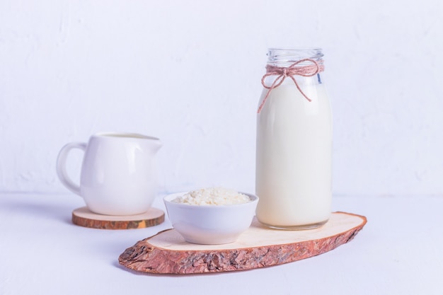 Vegan rice milk in a glass bottle and rice in a white plate on a wooden stand on a white background