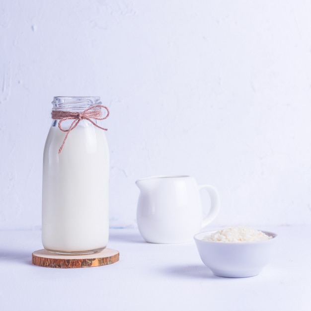 Vegan rice milk in a glass bottle and rice in a white plate on a wooden stand on a white background