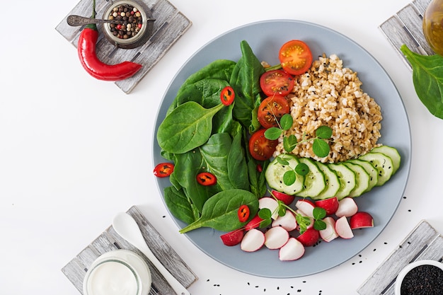 Vegan salad of fresh vegetables - tomatoes, cucumber, radish, spinach and oatmeal on bowl.