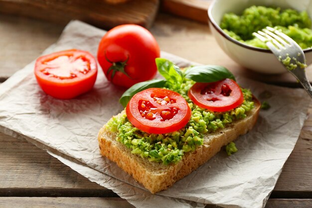 Vegan sandwich with avocado and vegetables on cutting board on wooden background